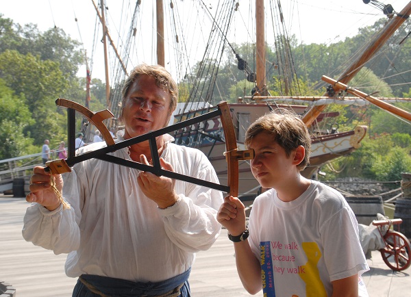 A Jamestown Settlement historical interpreter at the ships’ pier shows a visitor how to use a backstaff, a navigational tool used in the 17th century to measure the altitude of the sun or moon by the projection of a shadow. When observing the sun, users kept the sun to their back and observed the shadow cast by the upper vane on a horizon vane. (Courtesy Jamestown-Yorktown Foundation)