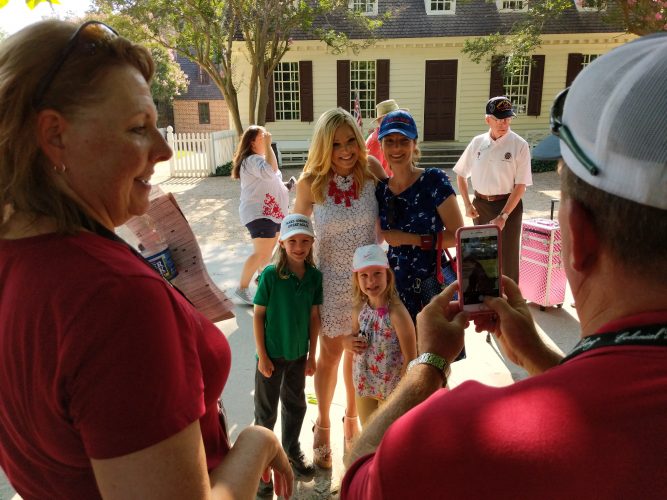 Gene and Karen Niston, of Texas, take a photo of Lois Stallman and her children with Fox News reporter Anna Kooiman. After seeing news on the internet about a Fox and Friends visit to the Historic Area, about a dozen protesters took to the Palace Green, carrying signs and occasionally shouting at Fox News crews. (WYDaily/Sarah Fearing)