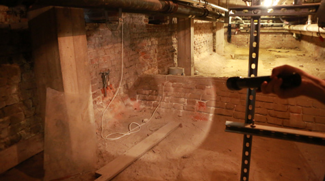 Susan Kern shines a flashlight on the place where the vaulted drain leads out of the Wren Building basement. (WYDaily/Courtesy of Stephen Salpukas)