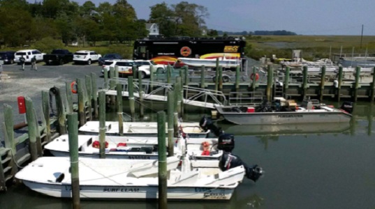 Vessels, including the VIMS landing craft RV Peregrination, prepare to transport communication gear to Parramore Island. The Suffolk Fire Department’s support bus (background) facilitates communication among responders using different frequencies and equipment. (Sean Fate/VIMS ESL/WYDaily