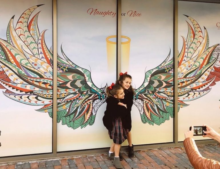 Visitors at City Center in Newport News pose for photo with wings painted onto a storefront. (WYDaily/Courtesy City Center at Oyster Point)